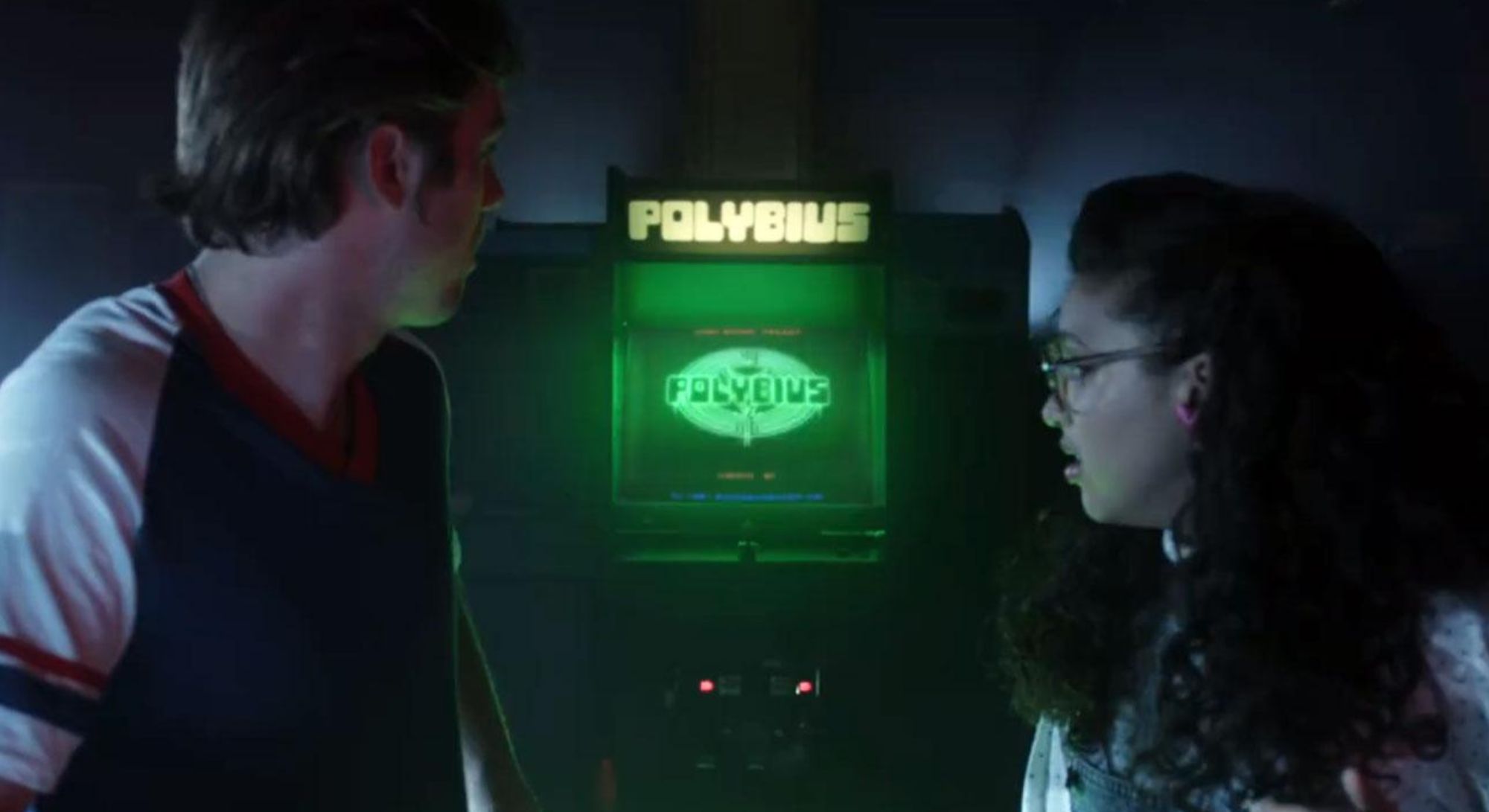 Polybius movie scene with a girl and boy in the foreground and Polybius game console at the back